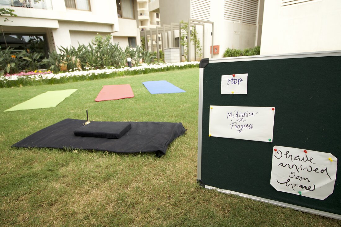 A quiet meditation setup on the lawn — mats, a bell, and a sign reading I have arrived, I am home