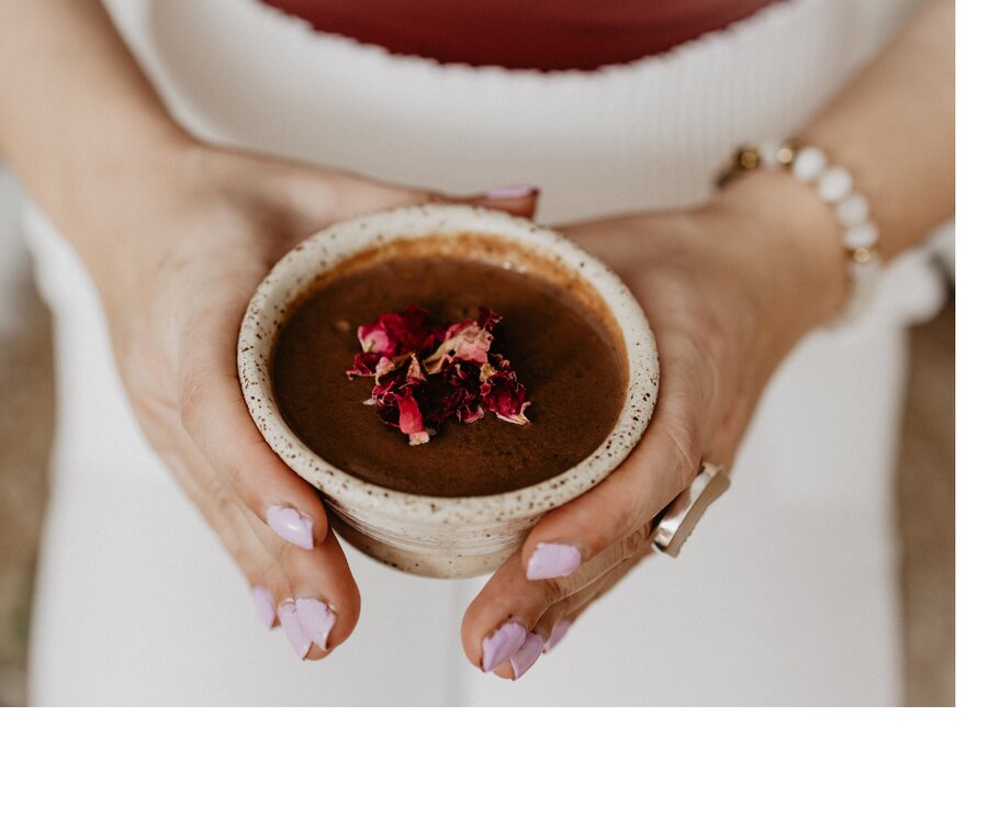 Hands holding a warm bowl of cacao topped with rose petals